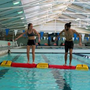 Two people on a Rolleo log in the pool.